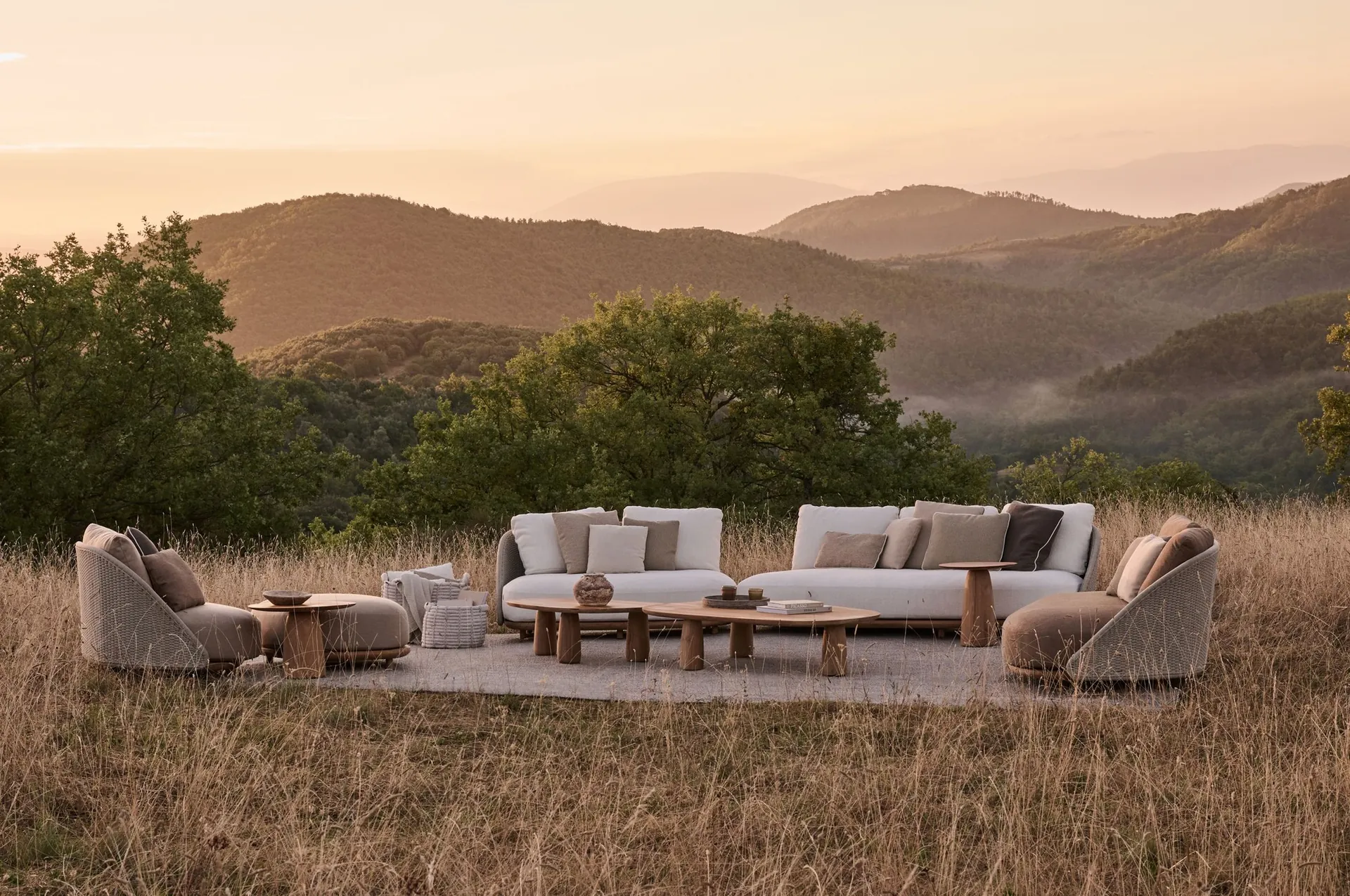 Tribù Elio curved sofas and lounge chairs on a rug in a hillside meadow