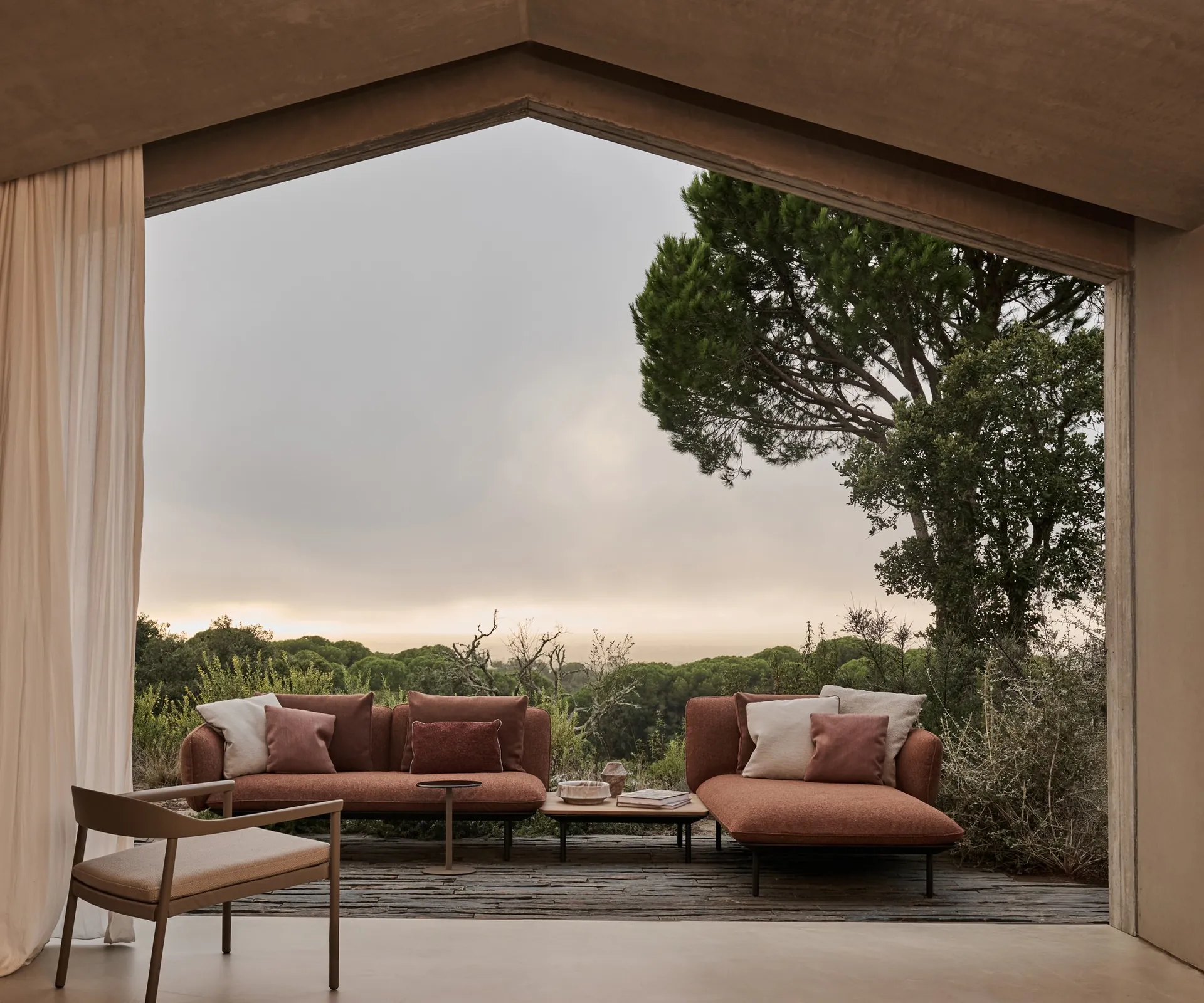 Tribù Illum lounge chair with terracotta sofas in a gabled pavilion open to pine trees