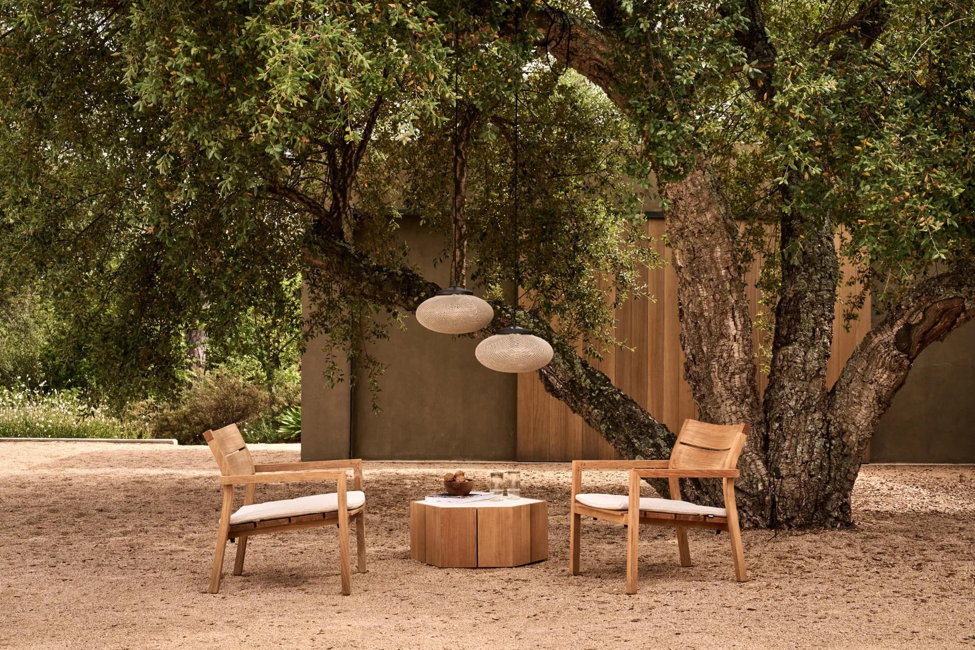 Two Tribù Kos teak lounge chairs and a round table under a large oak