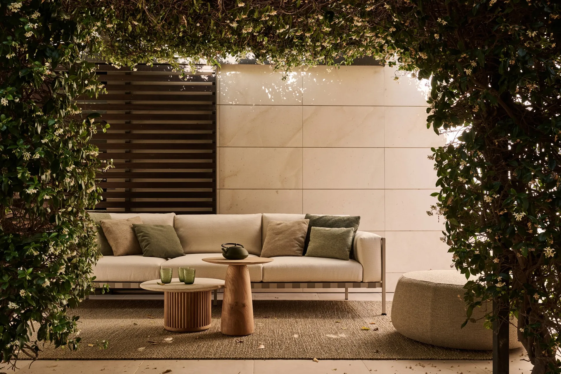 Tribù Natal Alu sofa with a side table and pouf under a vine-covered pergola
