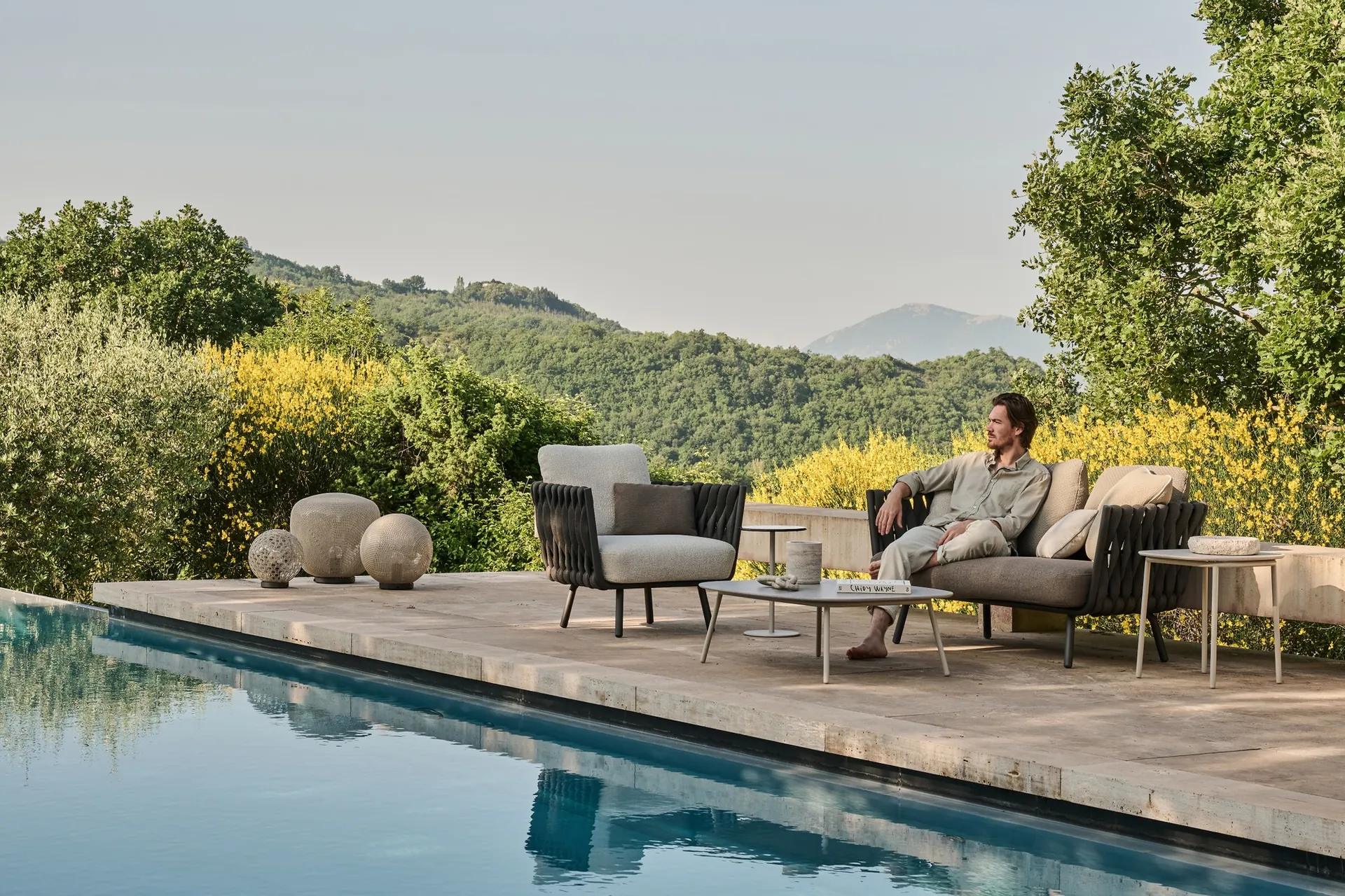 Man on a Tribù Tosca sofa beside a braided lounge chair at the edge of a pool